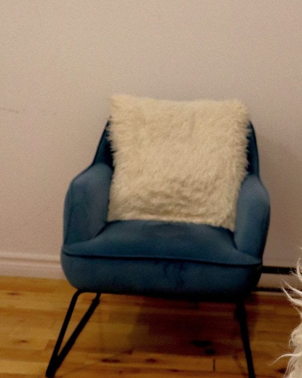 Le fauteuil bleu du cabinet de consultation, garni d’un coussin blanc à longs poils, sur un parquet clair.