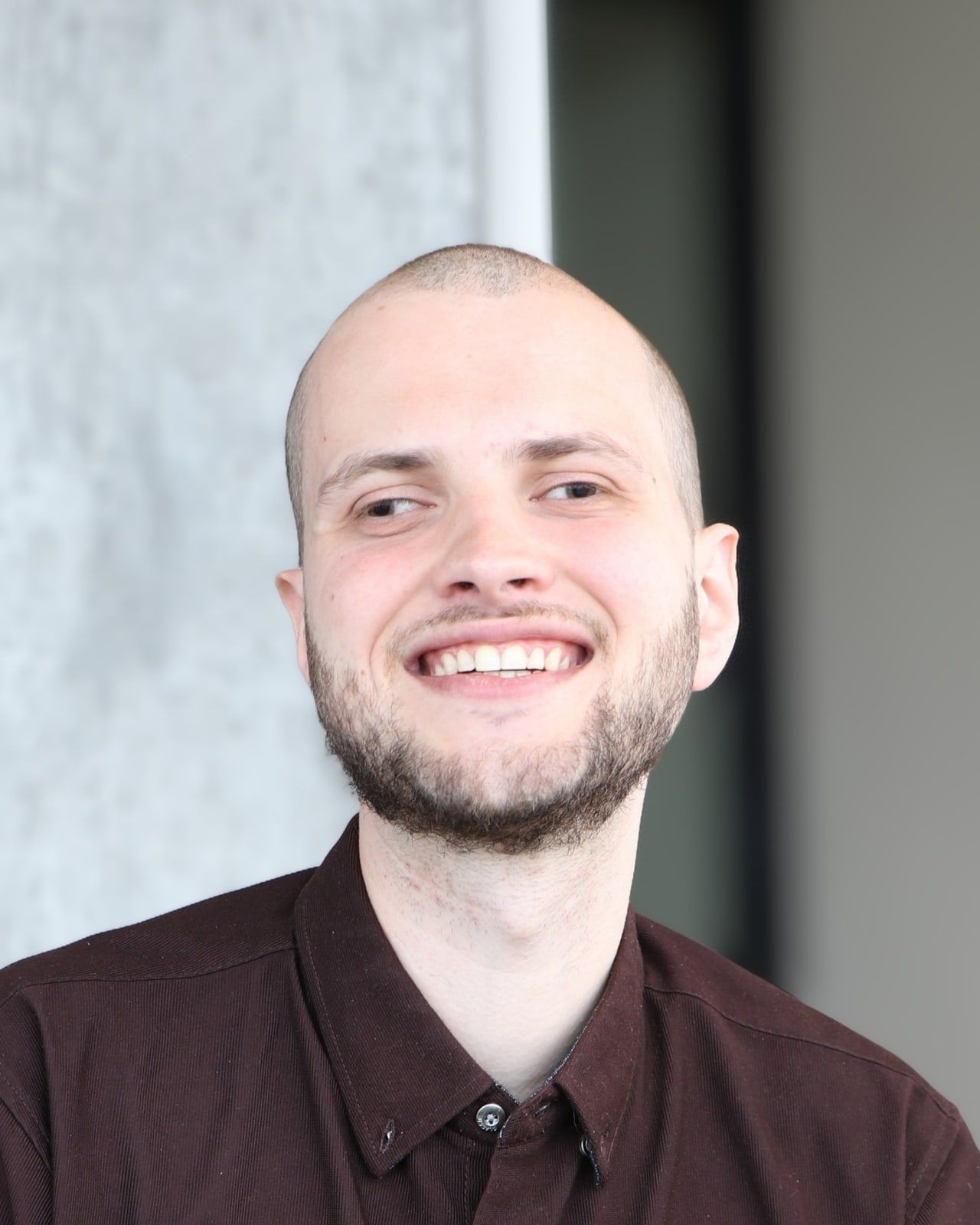 Marc de Montlivault, un grand sourire aux lèvres, regarde légèrement de côté. Il porte une chemise bordeaux et se tient devant un pilier de béton clair.